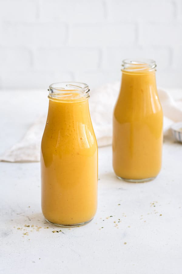 two yellow smoothies on a white counter with a white napkin 