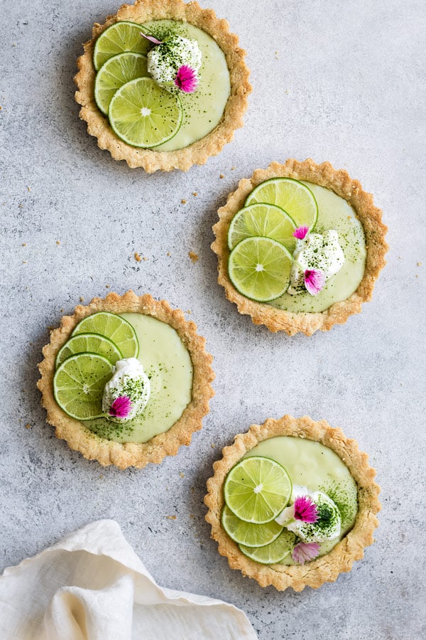 four mini vegan key lime pies with whipped coconut cream limes and flower petals on top