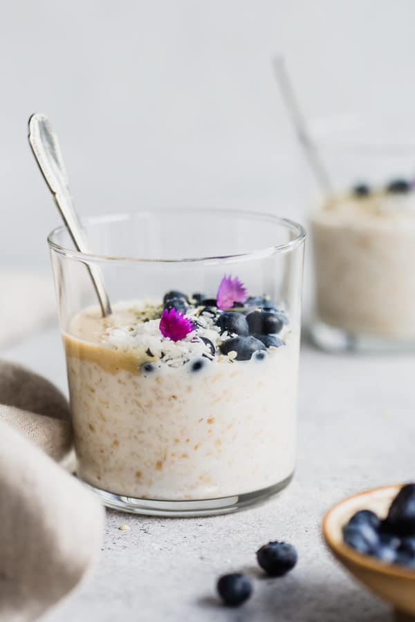 a cup of overnight steel cut oats topped with blueberries, shredded coconut and hemp seeds