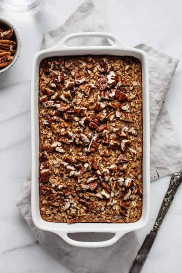 Pecan pie baked oatmeal in a white baking dish with a knife on the side