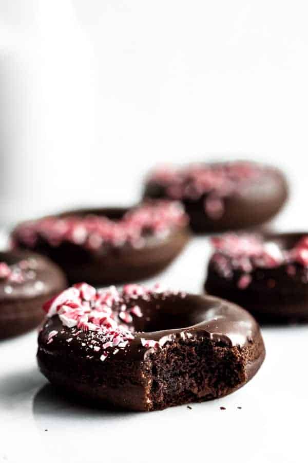 A peppermint mocha donut topped with crushed candy canes with a bite taken out of it
