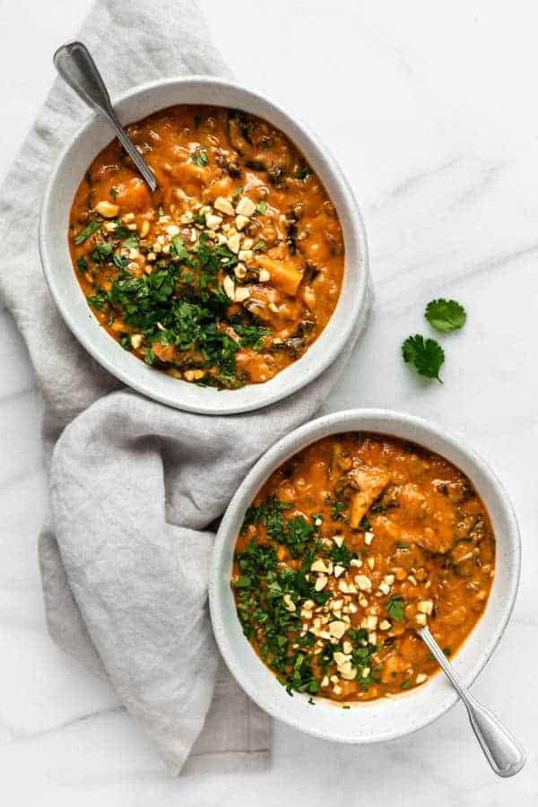 Two bowls of west African peanut stew with spoons in them topped off with crushed peanuts and cilantro