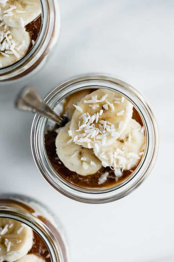 small jars filled with chia pudding, bananas, yogurt and caramel sauce