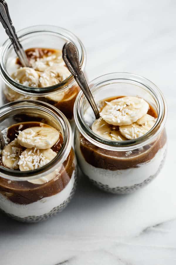 small jars filled with chia pudding, bananas, yogurt and caramel sauce