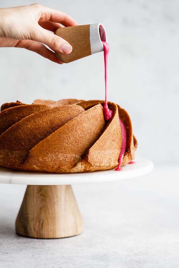 an orange cardamom bundt cake on a cake stand with pink blood orange glaze and chopped pistachios