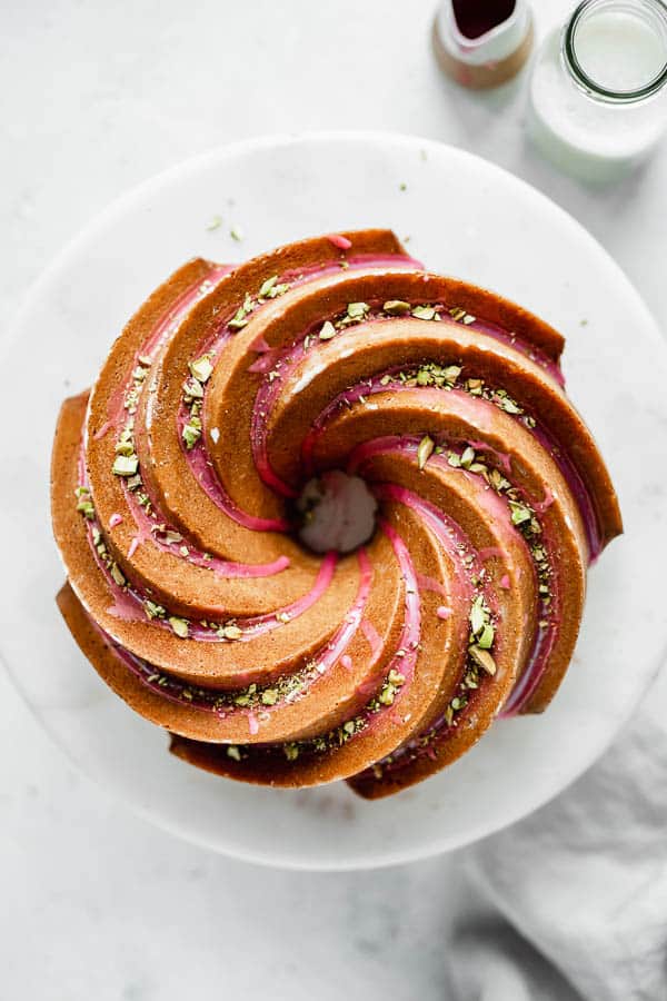 an orange cardamom bundt cake on a cake stand with pink blood orange glaze and chopped pistachios