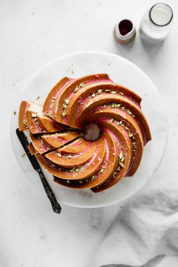 an orange cardamom bundt cake on a cake stand with pink blood orange glaze and chopped pistachios