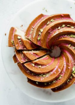 an orange cardamom bundt cake on a cake stand with pink blood orange glaze and chopped pistachios