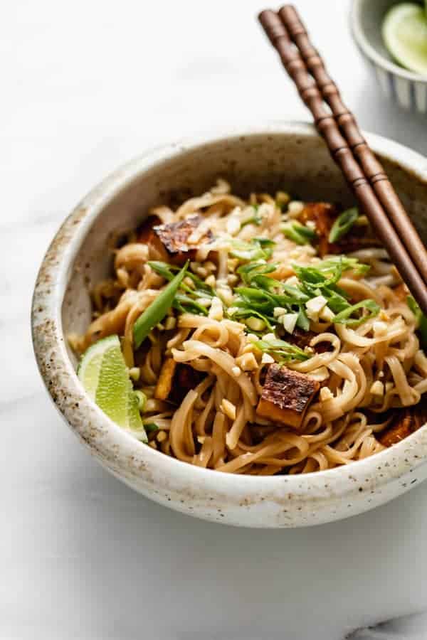 vegan pad thai in a ceramic bowl with sliced scallions and a wedge of lime
