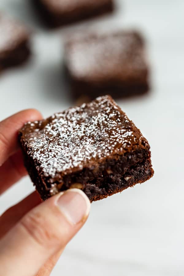 a hand holding a fudge brownie topped with powdered sugar