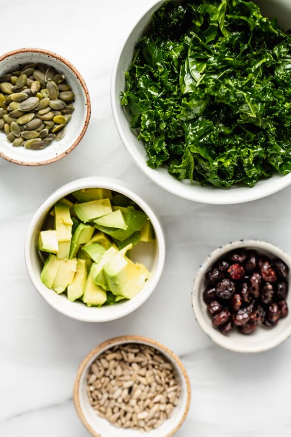 ingredients for a massaged kale salad with kale, avoacdo, cranberries, and pumpking seeds