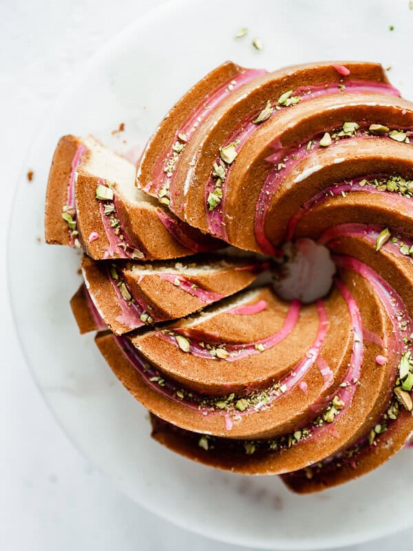 an orange cardamom bundt cake on a cake stand with pink blood orange glaze and chopped pistachios