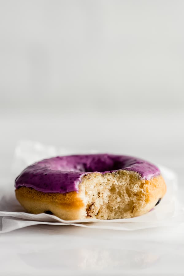 A close up of a blueberry donut with blueberry glaze with a bite taken out of it