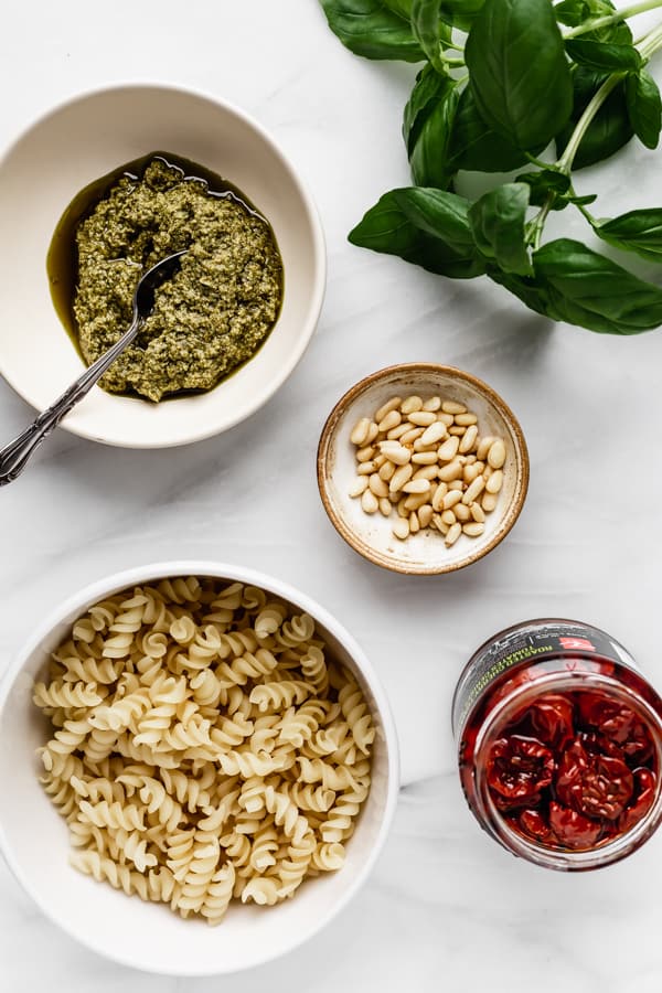 pesto, basil, pine nuts, sun-dried tomatoes and pasta on a marble board