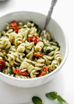 a close up image of a bowl of pesto pasta salad