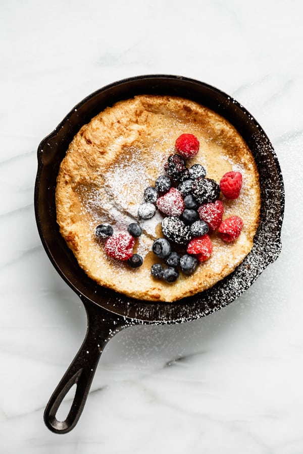 Dutch baby pancake in a cast iron skillet topped with berries and powdered sugar