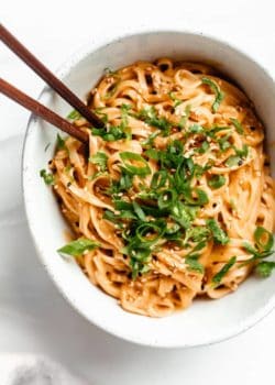 a bowl of red curry noodles topped with green onion and cilantro