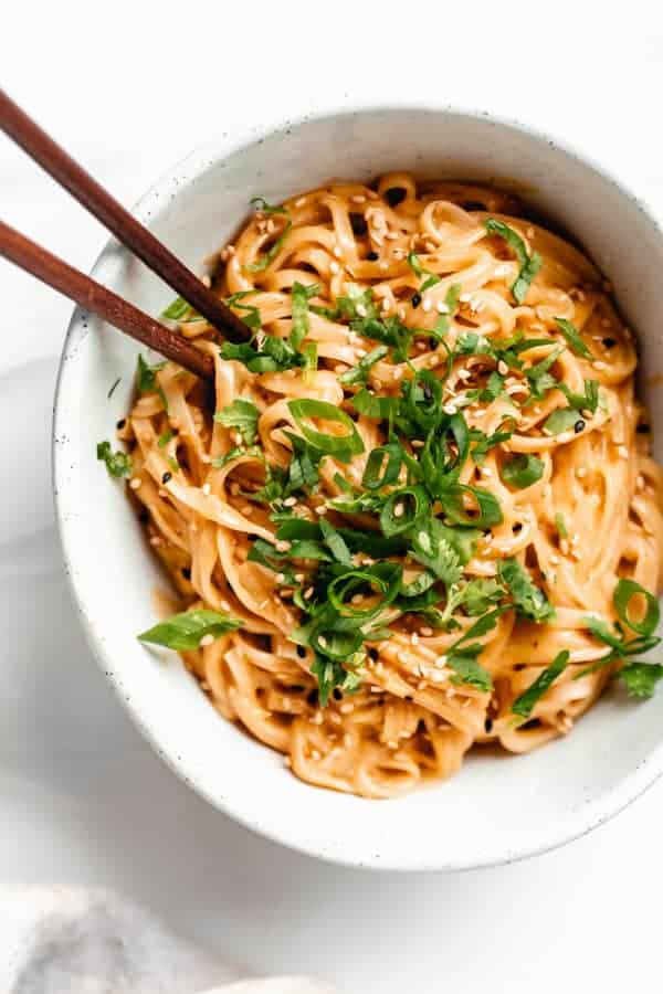 a bowl of red curry noodles topped with green onion and cilantro