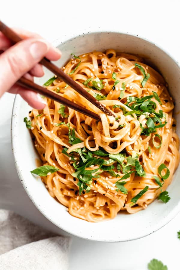 a hand using chopsticks to pick up a bite of red curry noodles from a bowl