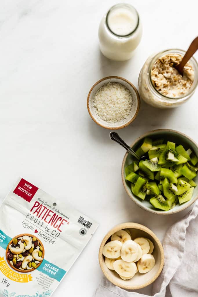 a flat lay of almond milk, coconut, muesli, kiwis, and bananas