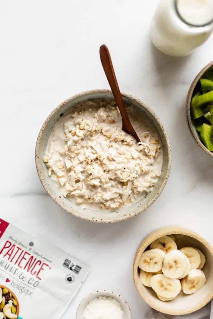 a bowl of bircher muesli with some almond milk, kiwis, and bananas on the side
