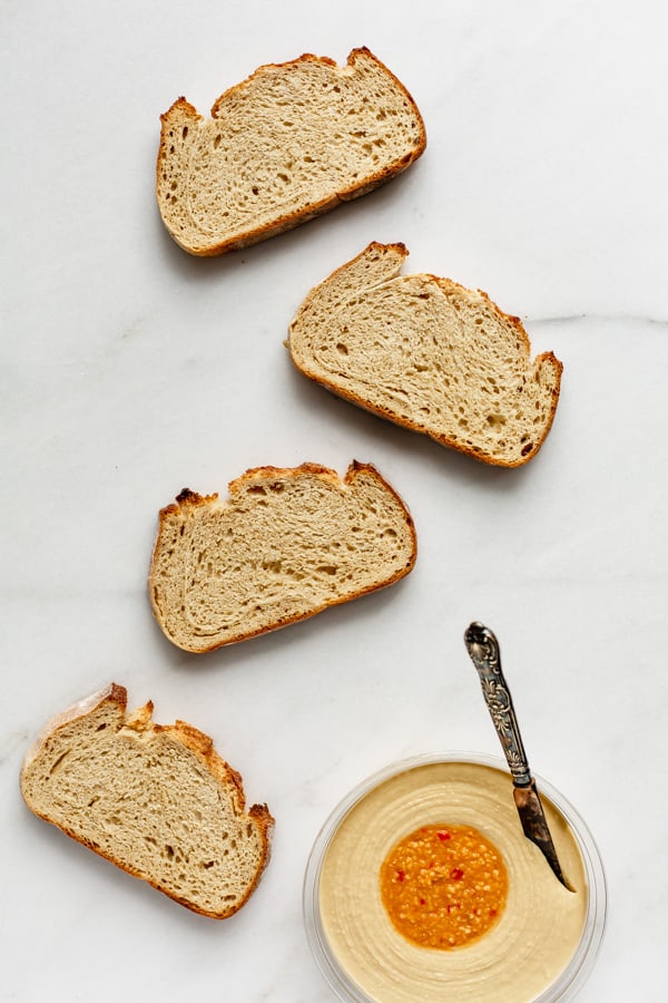 four pieces of toast with a container of hummus on the side