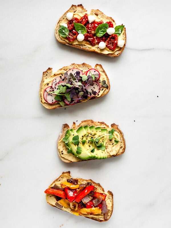 4 pieces of toast with vegetable toppings on a marble board