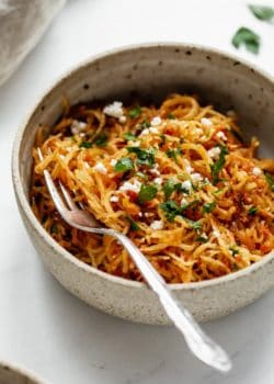 a close up of sun dried tomato spaghetti squash in a ceramic bowl