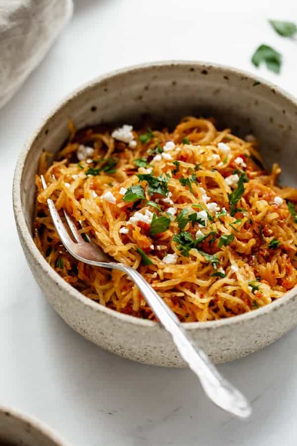 a close up of sun dried tomato spaghetti squash in a ceramic bowl