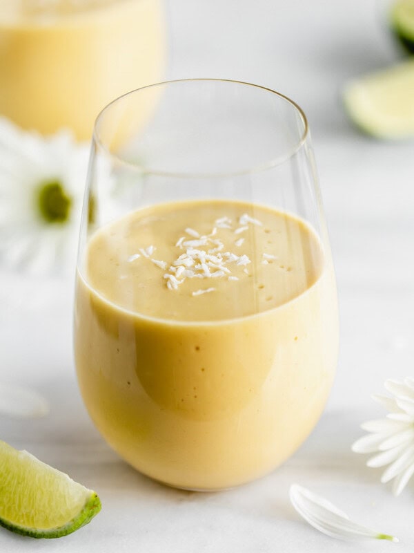 a glass of vegan mango lassi on a marble board with limes and flowers