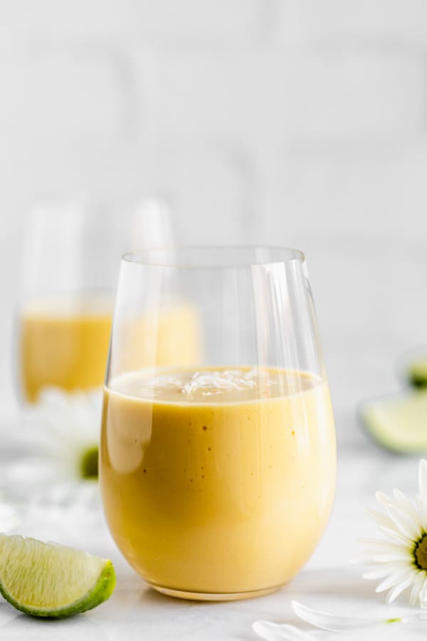 a glass of vegan mango lassi with shredded coconut on top