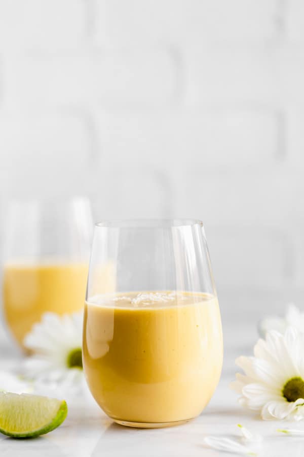 a glass of vegan mango lassi with flowers in the background