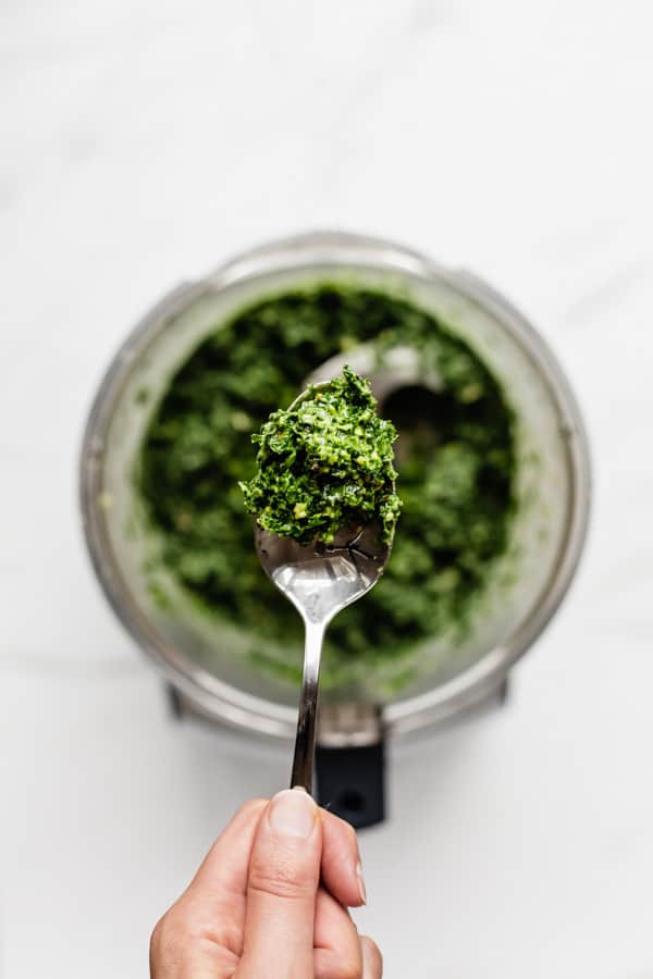 a hand holding a spoon of kale pesto