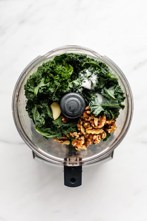 a food processor with kale, walnuts, garlic and salt in it