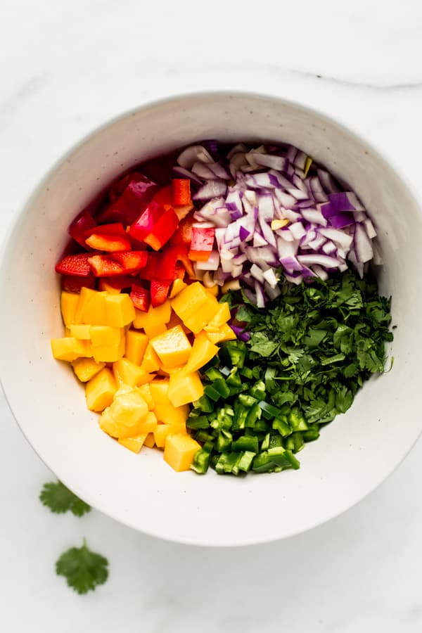 a mixing bowl with mango salsa ingredients in small piles