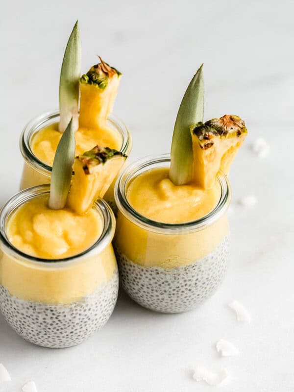 3 jars of pina colada chia pudding with pineapple wedges in them on a marble board