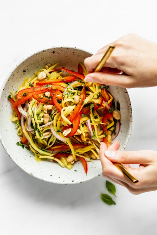 two hands tossing a bowl of mango salad