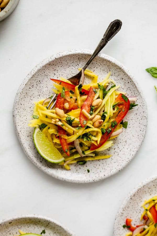 a white plate with mango salad and a lime wedge