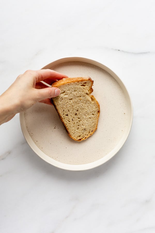 a piece of bread being dunked into a bowl of vegan french toast liquid
