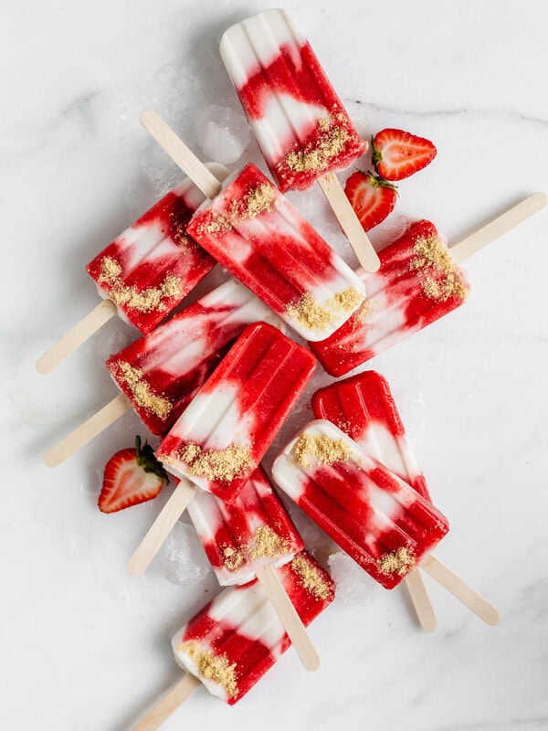a top down view of a bunch of vegan strawberry cheesecake popsicles on a marble board