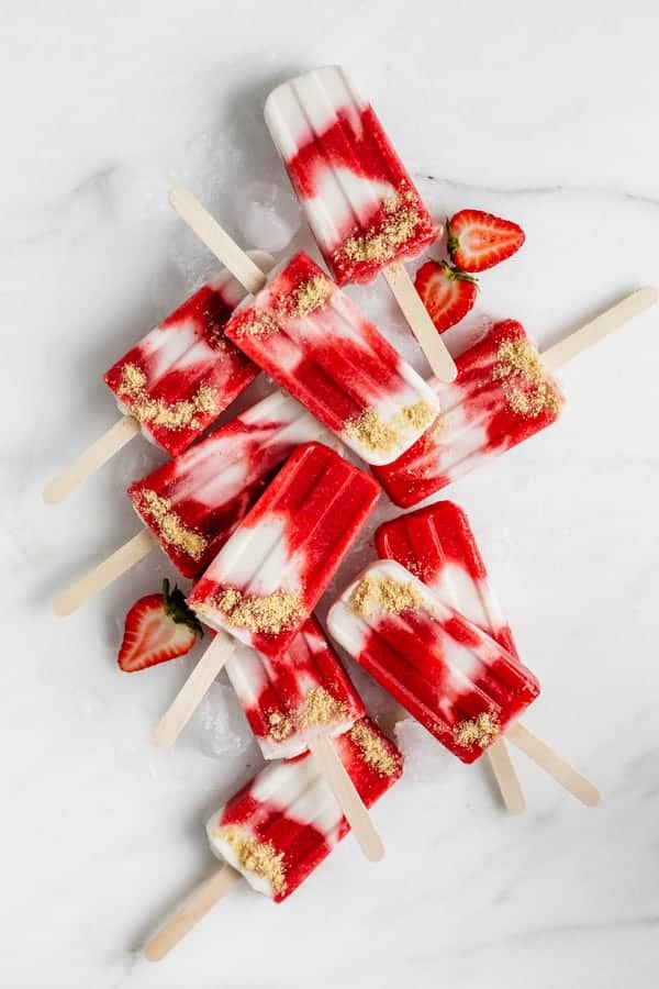 a top down view of a bunch of vegan strawberry cheesecake popsicles on a marble board