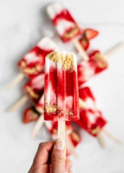 a hand holding a strawberry cheesecake popsicle
