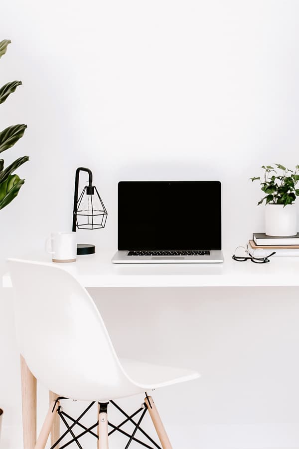 A white desk with a Macbook, cup of coffee and a plant on it