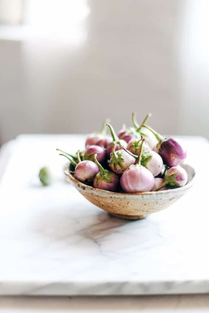 A bowl of small eggplant on a white marble background