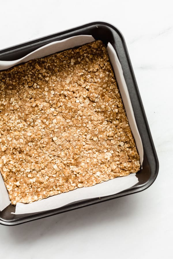 an 8x8 inch pan with apple pie bars crumble mixture pressed down in it