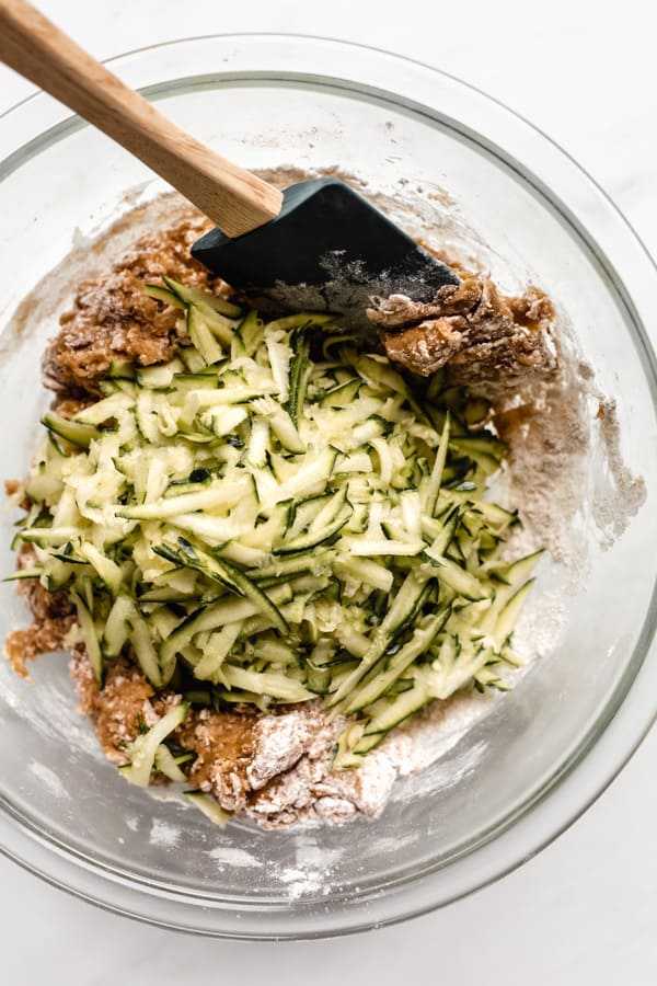 zucchini bread batter with a pile of grated zucchini on top in a clear mixing bowl