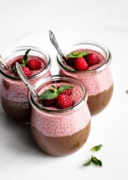 three cups of chocolate and raspberry chia pudding topped with raspberries and fresh mint