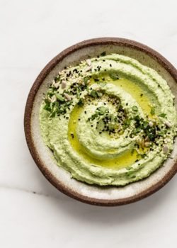edamame hummus topped with olive oil, seeds and chopped cilantro on a brown ceramic plate