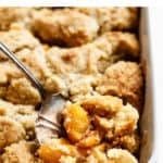 peach cobbler in a porcelan baking dish with a scoop being taken out