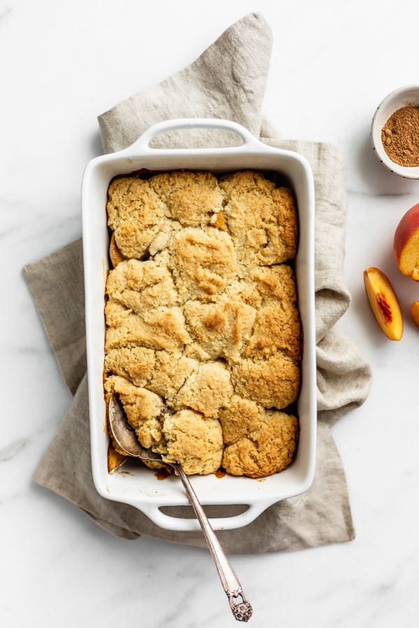 a white baking dish of peach cobbler on a beige linen napkin